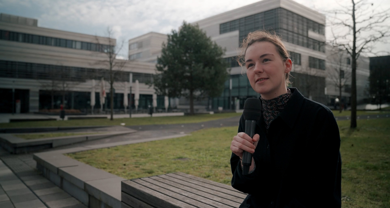 Eine Studentin mit Mikrophon erzählt von Erfahrungen mit Digitalisierung, sitzend im Hof der Hochschule 